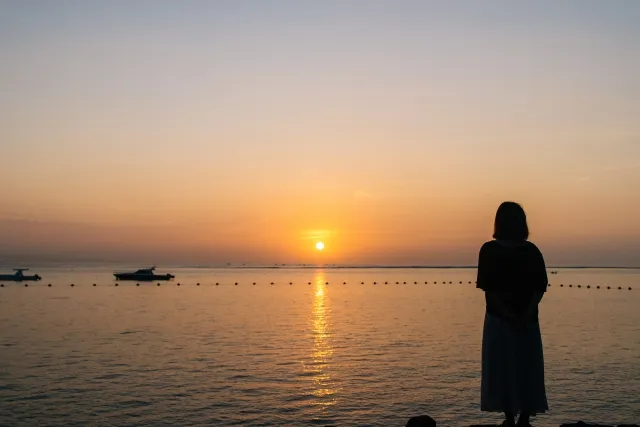 夕日の海に向かって立つ女性のシルエット